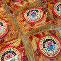 Several individually wrapped cornbread squares with red chili sauce, each topped with a circular 'Sweet Chili Cornbread' label from Tablecloth Bakery, arranged closely together.